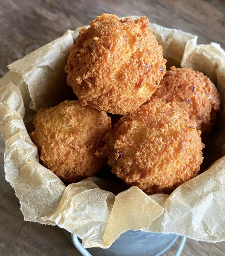 Round crispy hushpuppies in a small metal bucket with natural parchment paper.