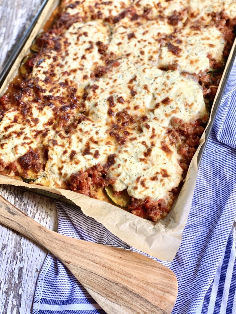 Sheet pan zucchini lasagna on a blue striped hand towel and a wood spatula to use to serve it with.