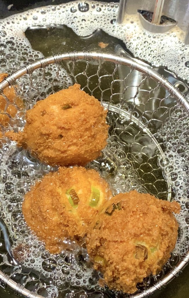 3 golden brown hushpuppies being lifted from the hot oil.