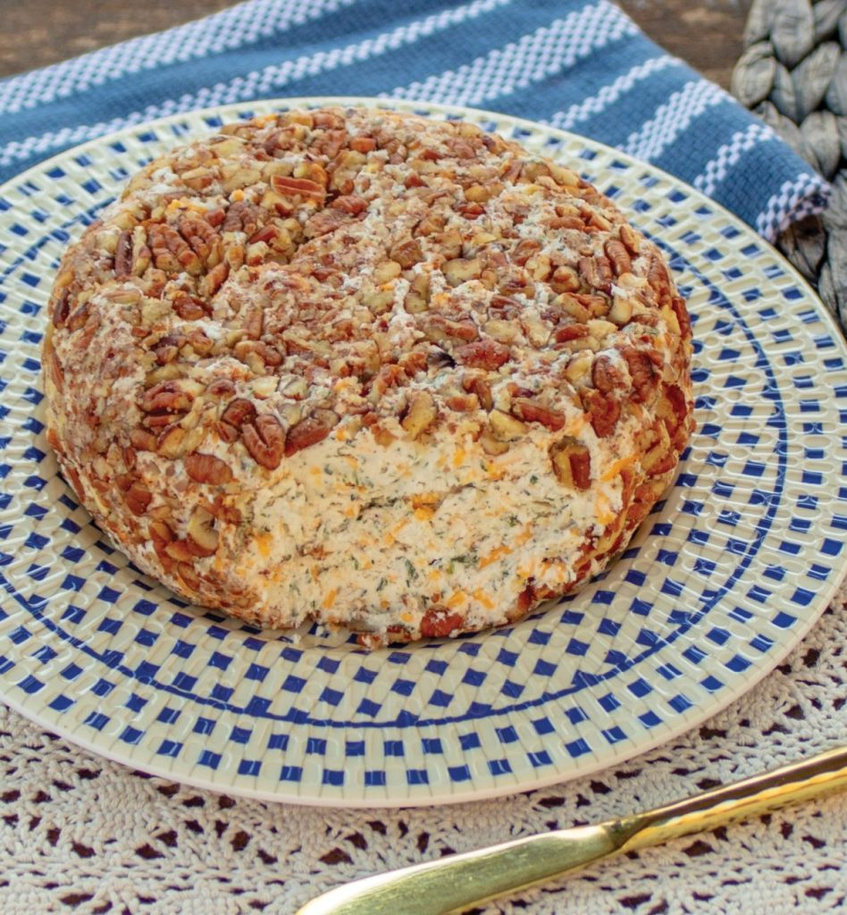 Low carb cheddar ranch cheeseball on a blue and white checkered plate. There's a small gold cheese knife for serving.