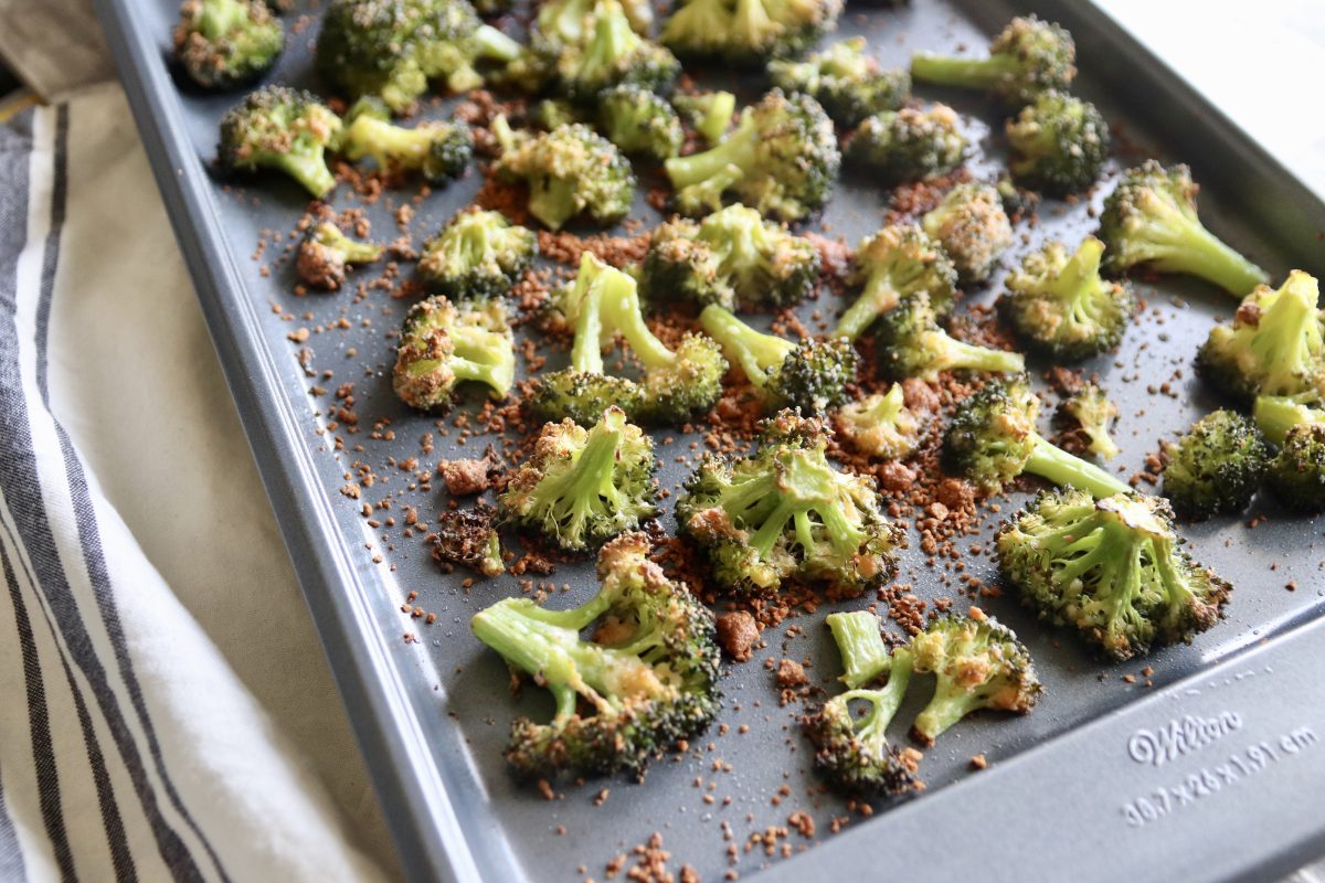 A sheet pan with cooked parmesan roasted broccoli. It's sitting on a gray and cream striped hand towel.