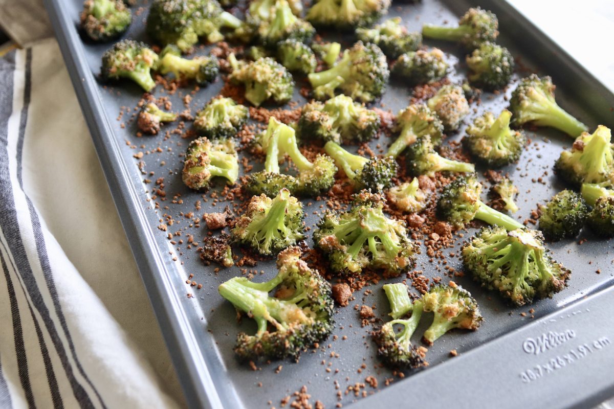 A sheet pan with cooked parmesan roasted broccoli.  It's sitting on a gray and cream striped hand towel.