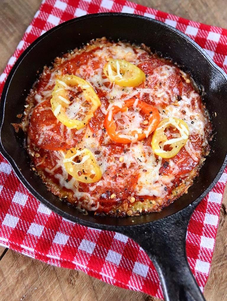 A personal pan pizza in a mini cast iron skillet. It's sitting on a red and white gingham cloth napkin.