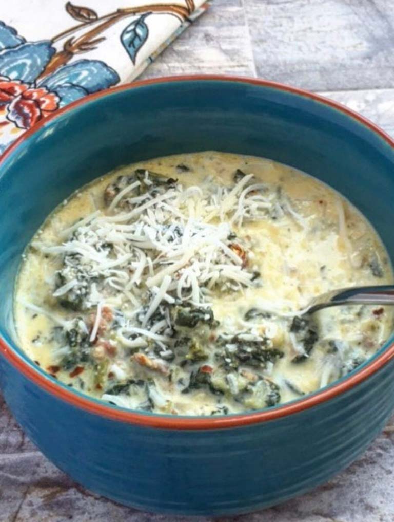 A blue bow filled with keto zuppa toscana soup. A floral cloth napkin to the left of the bowl.