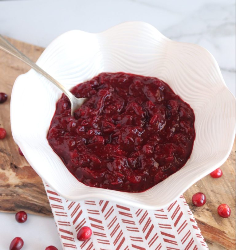 A decorative white bowl with sugar free cranberry sauce and a spoon. It's on a red and white hand towel.