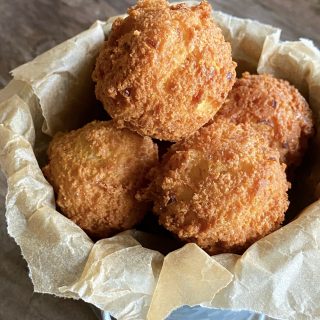 Round crispy hushpuppies in a small metal bucket with natural parchment paper.