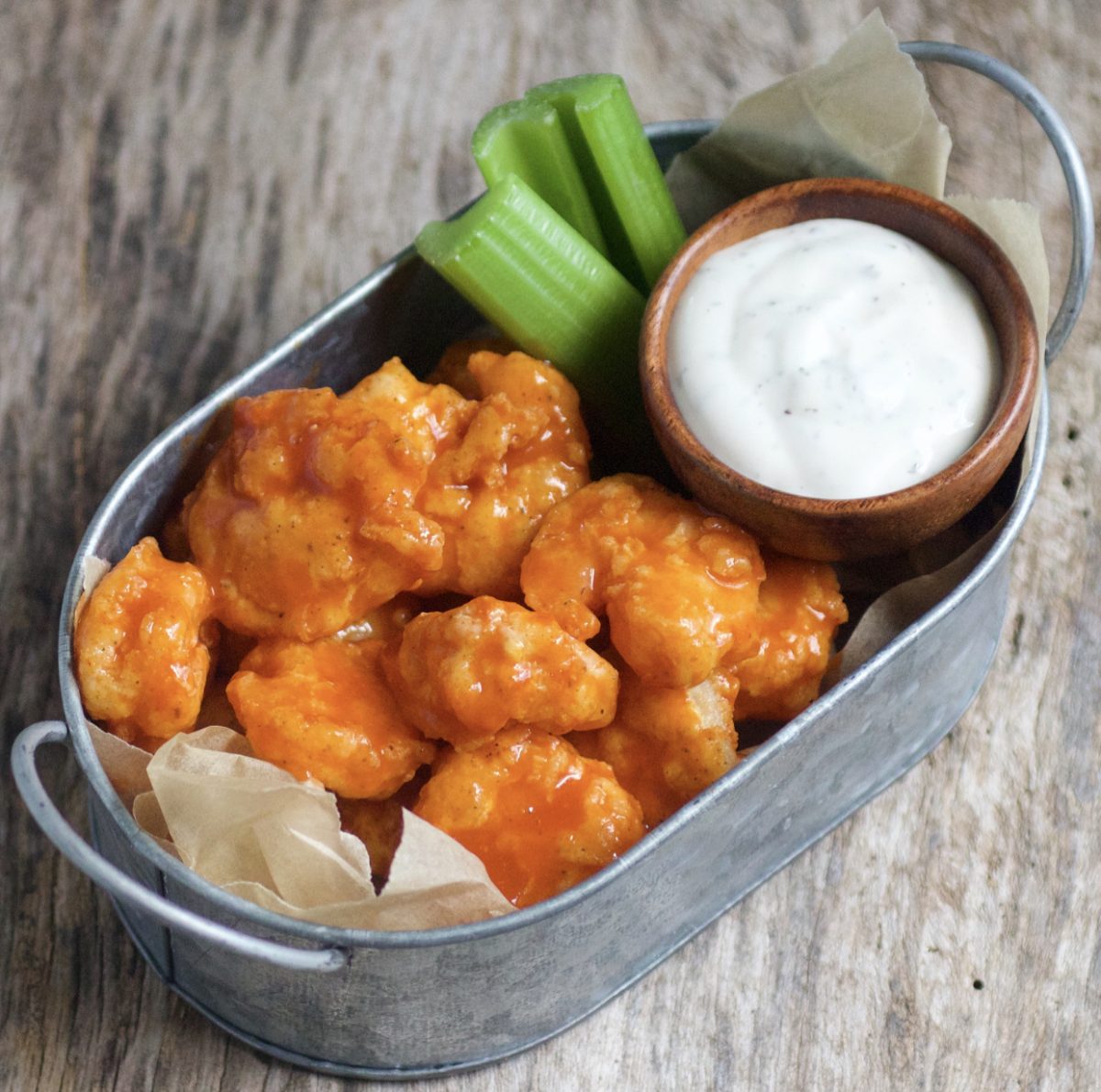 Buffalo shrimp with ranch dressing and celery sticks, served in a small tin bucket.