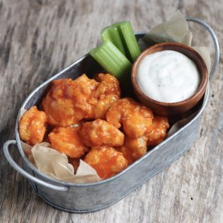 Buffalo shrimp in a tin bucket with celery and ranch dressing. The dressing is served in a small round wooden bowl.