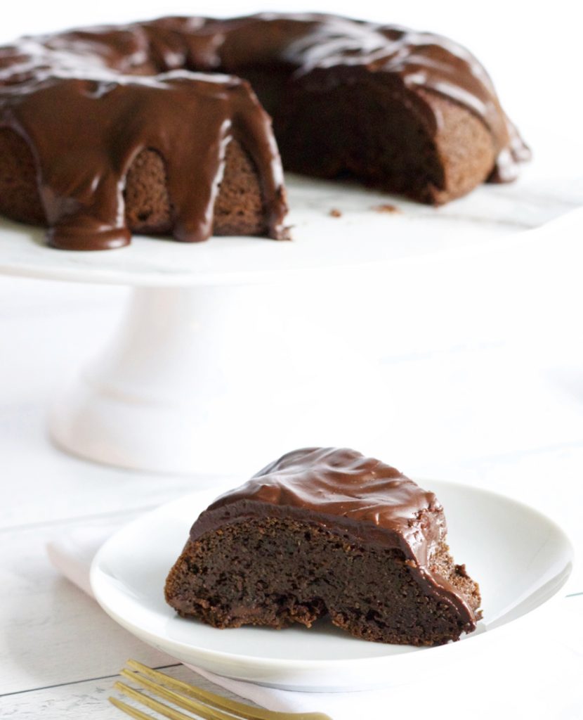 Chocolate cake on a stand.  one pice of chocolate cake on a plate beside the stand.