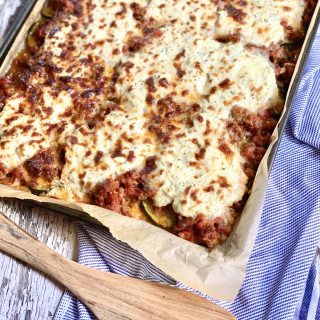 Sheet pan zucchini lasagna on a blue striped hand towel and a wood spatula to use to serve it with.