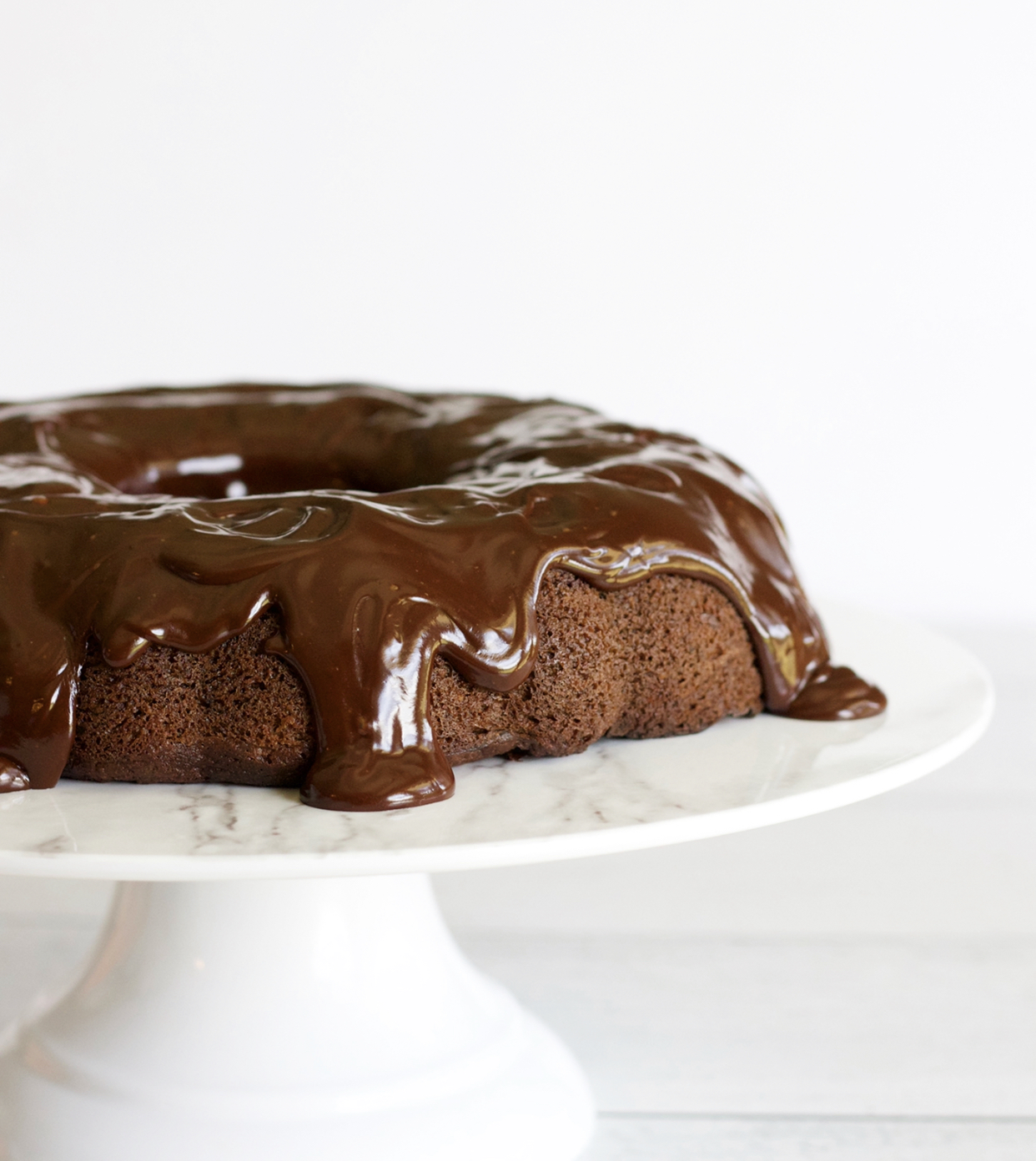 Chocolate cake with chocolate ganache on a white cake stand.