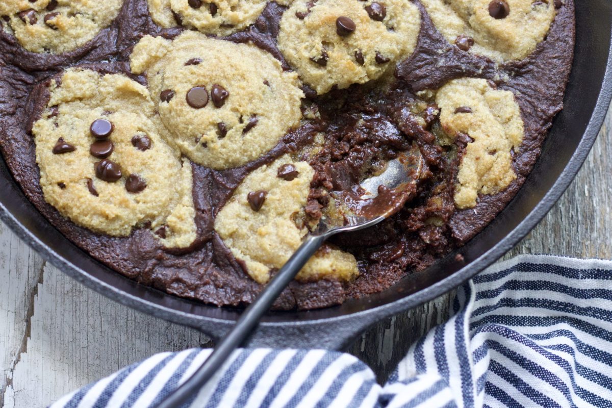 A cast iron skillet with a keto chocolate chip[ brookie in it. A blue and white striped hand towel is laying beside it.  