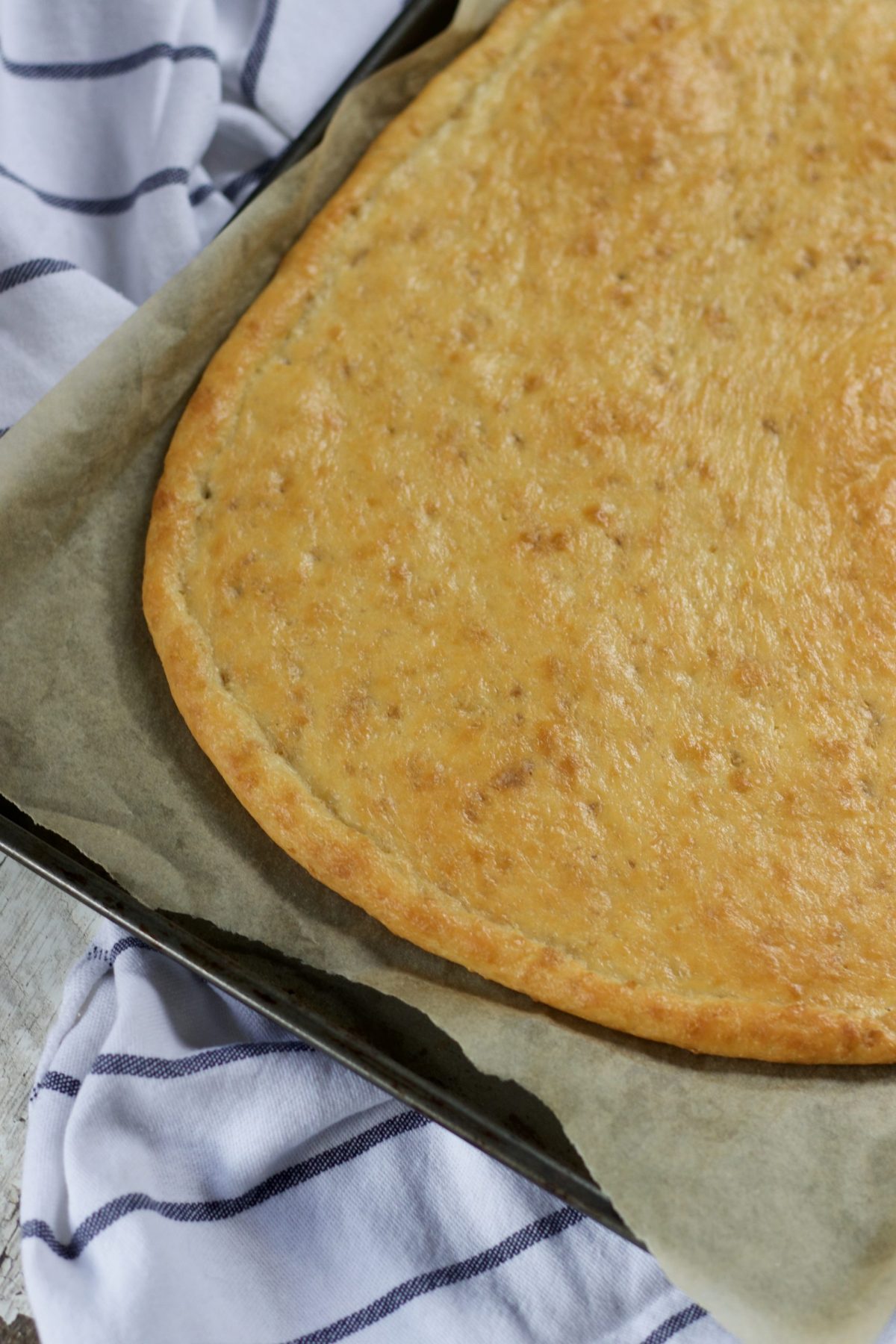 Pizza crust on a metal baking sheet.  The baking sheet is sitting on a blue and white striped hand towel.