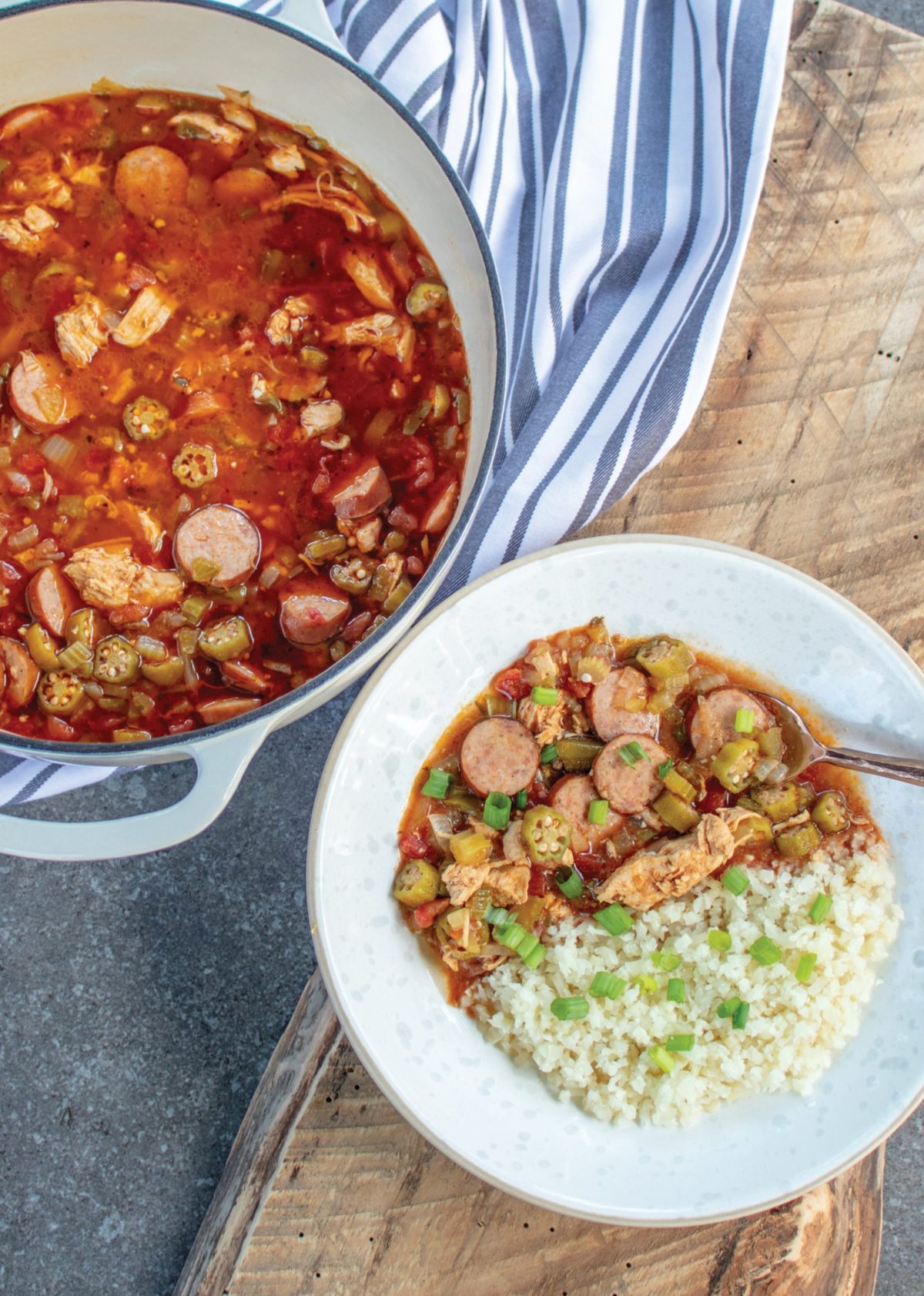 A white dutch oven with gumbo in it. A bowl of gumbo and cauliflower rice.