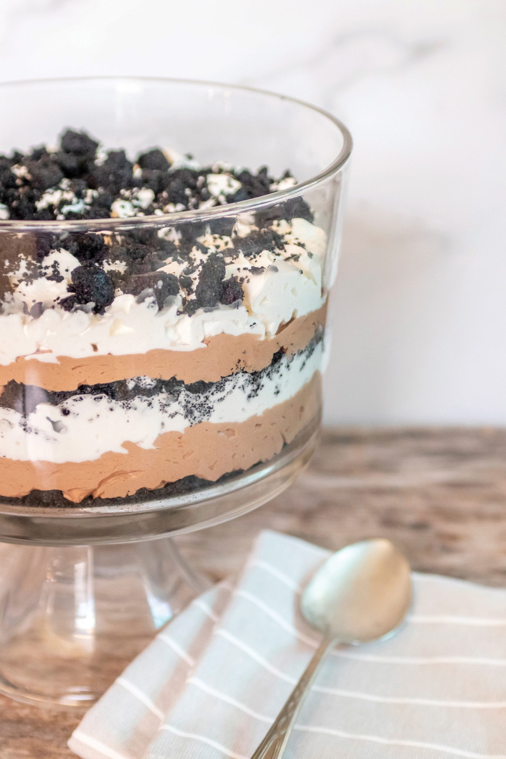 Dirt cake in a clear glass trifle bowl. serving spoon and light gray and white striped napkin.