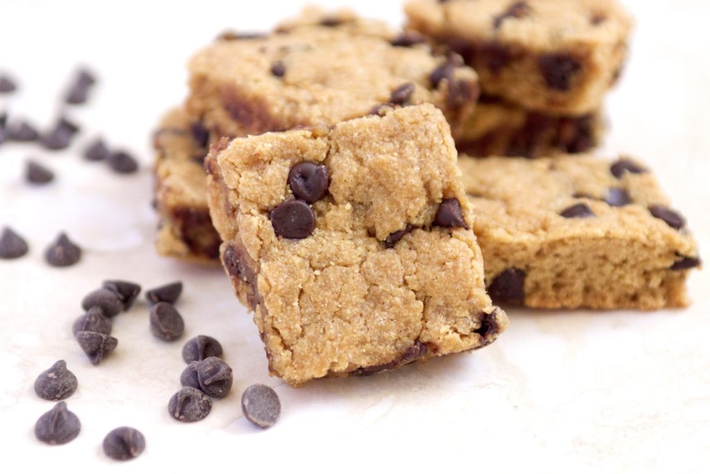 Low carb flourless peanut butter chocolate chip cookie bars stacked. There are chocolate chips scattered around them.