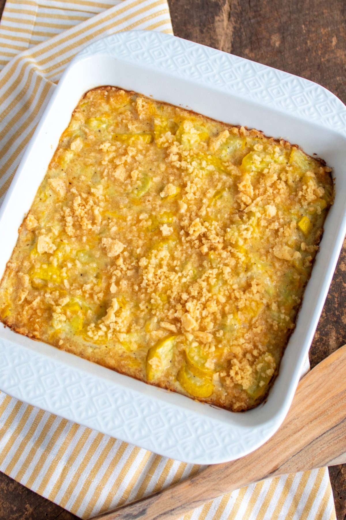 A square white casserole dish with squash casserole. The dish is sitting on a yellow and white striped napkin.