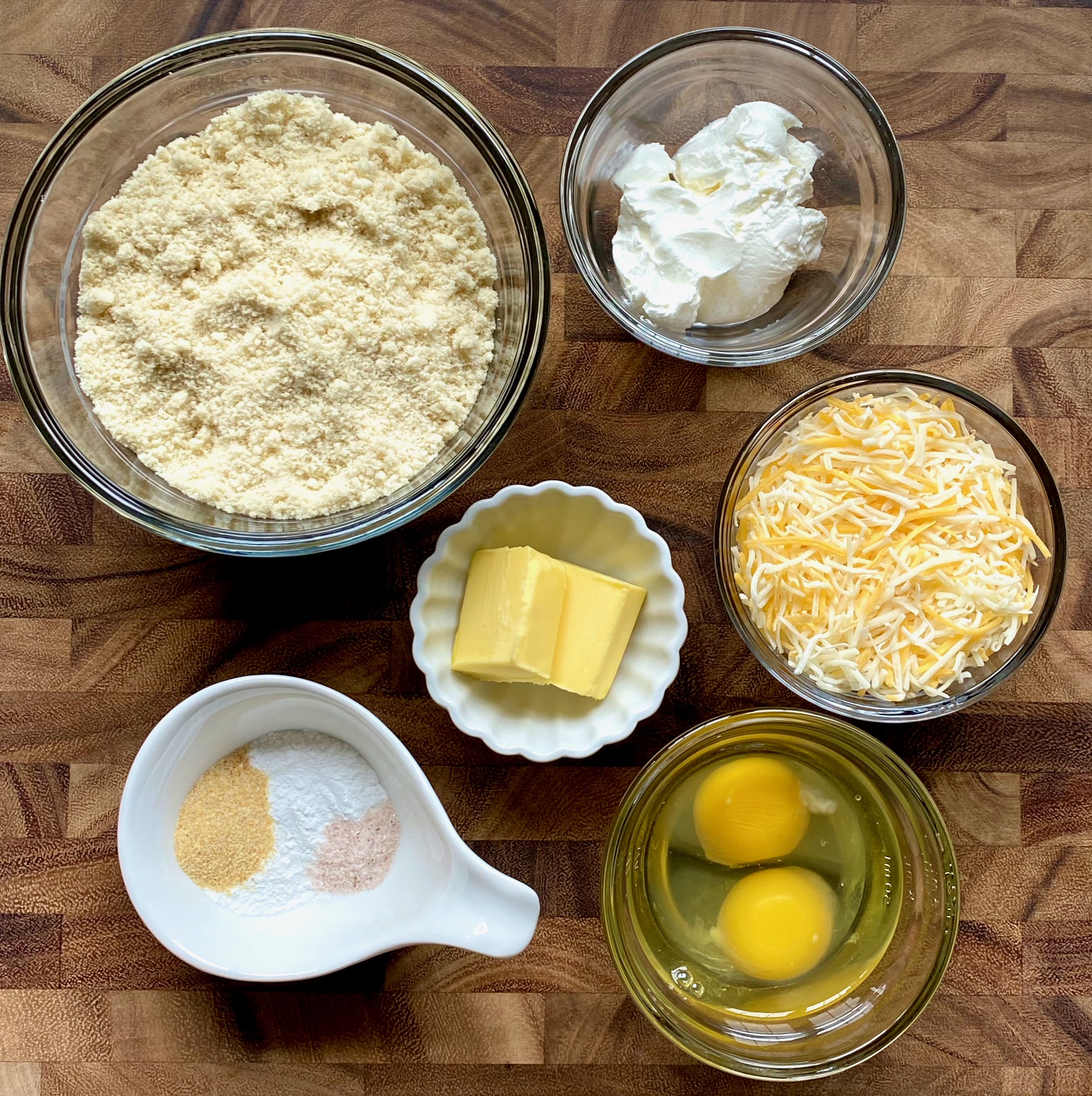 Ingredients for cheese biscuits in bowls Almond flour, baking powder, garlic powder, salt, butter, eggs and sour cream.