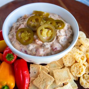 a white bowl of sausage dip topped with jalapeños. peppers, low carb crackers and parmesan crisps for dipping.