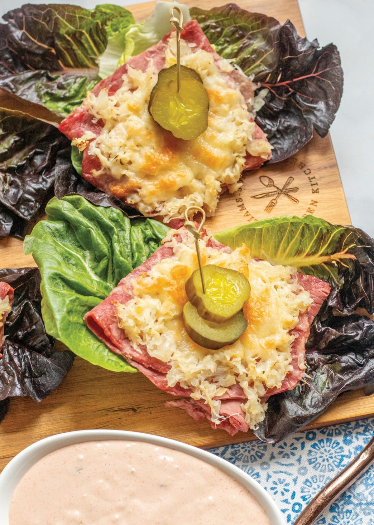 Reuben lettuce wraps. Lettuce boats topped with corned beef, swiss cheese and pickles. a white bowl of Reubin dressing.