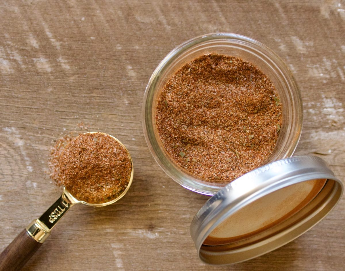 a jar and a measuring spoon containing  homemade creole seasoning.