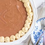 peanut butter chocolate pie in a white ceramic pie plate. a blue and white plate sitting on a tan cloth napkin. two dessert forks