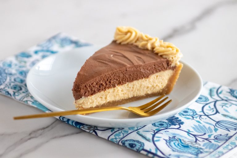 a slice of chocolate peanut butter pie ona white plate on a blue and white napkin. a gold dessert fork.