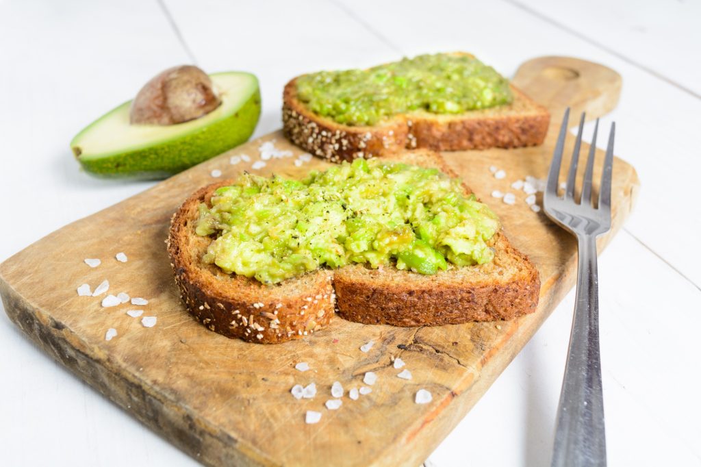 Avocado toast on a wooden board with a fork.
