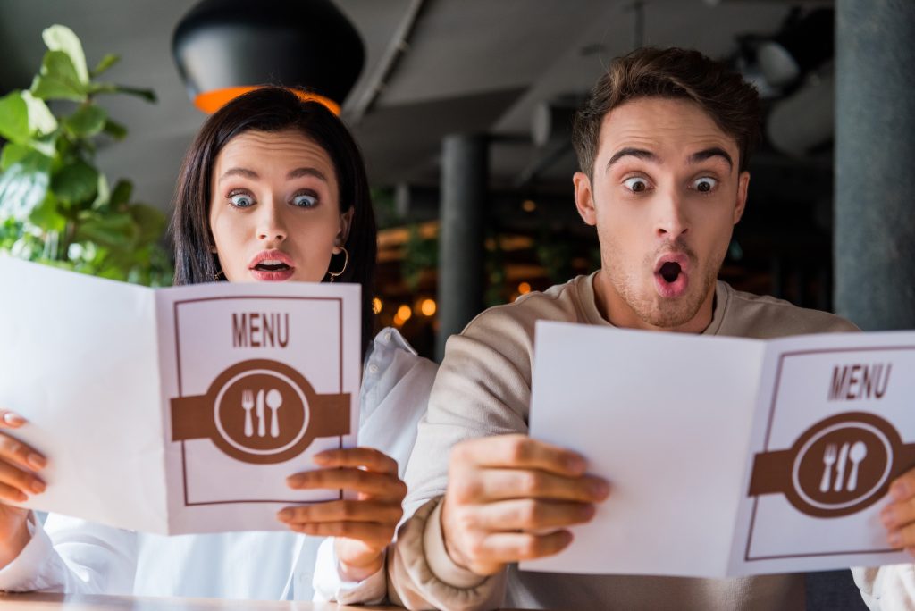 Man and woman with menus in their hands and suprised look on their faces.