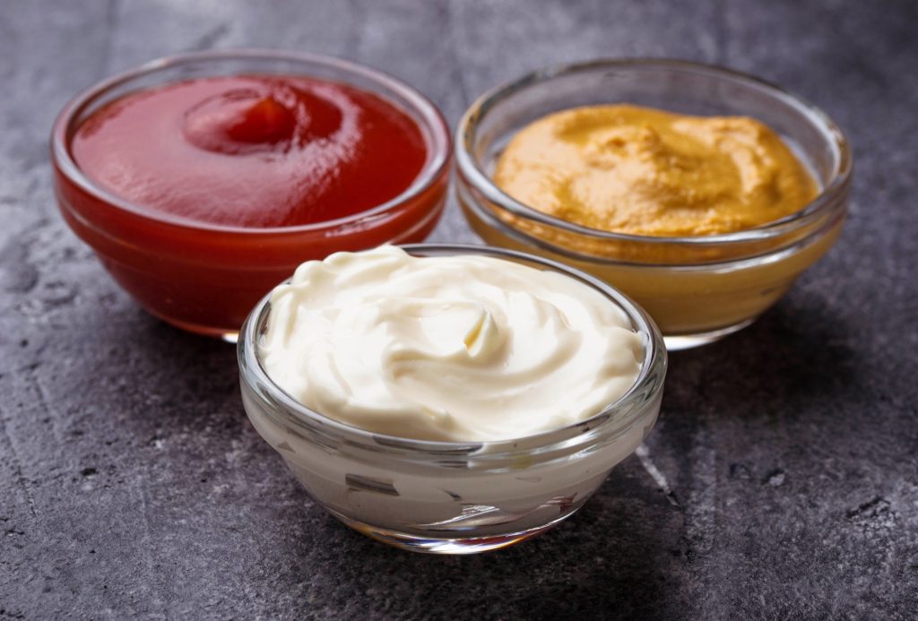 Condiments in small glass bowls.  Mustard, mayonnaise and ketchup.