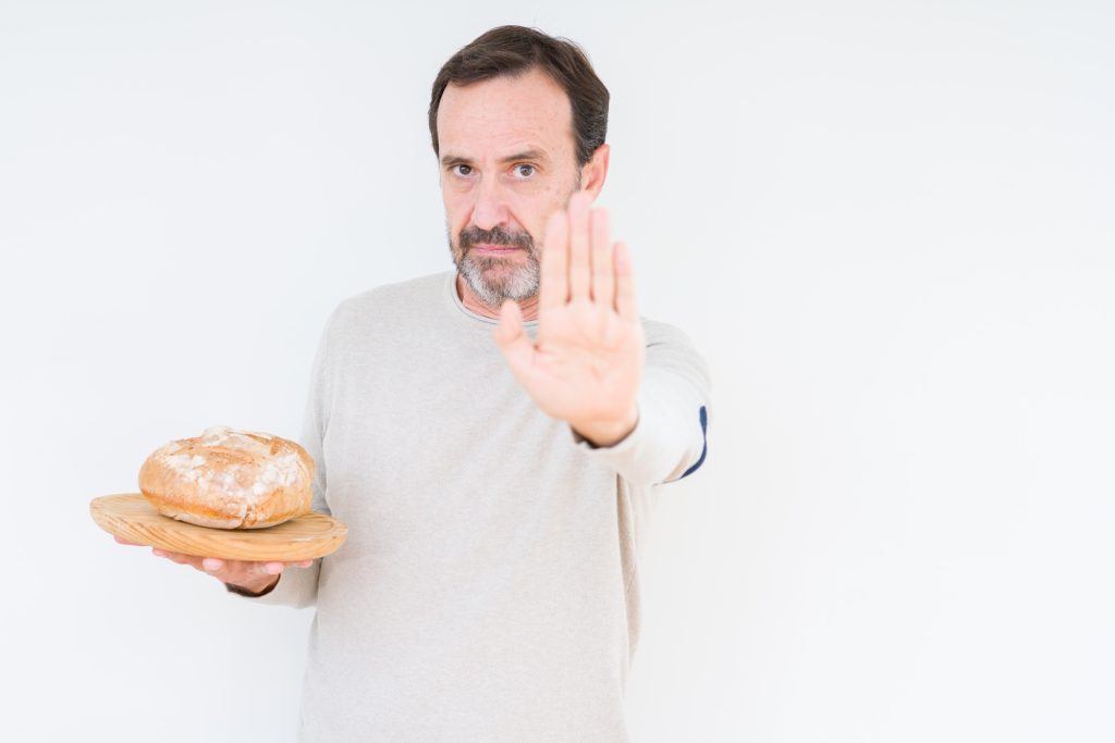 Man holding bread and with the other hand holding up as if to say, stop.