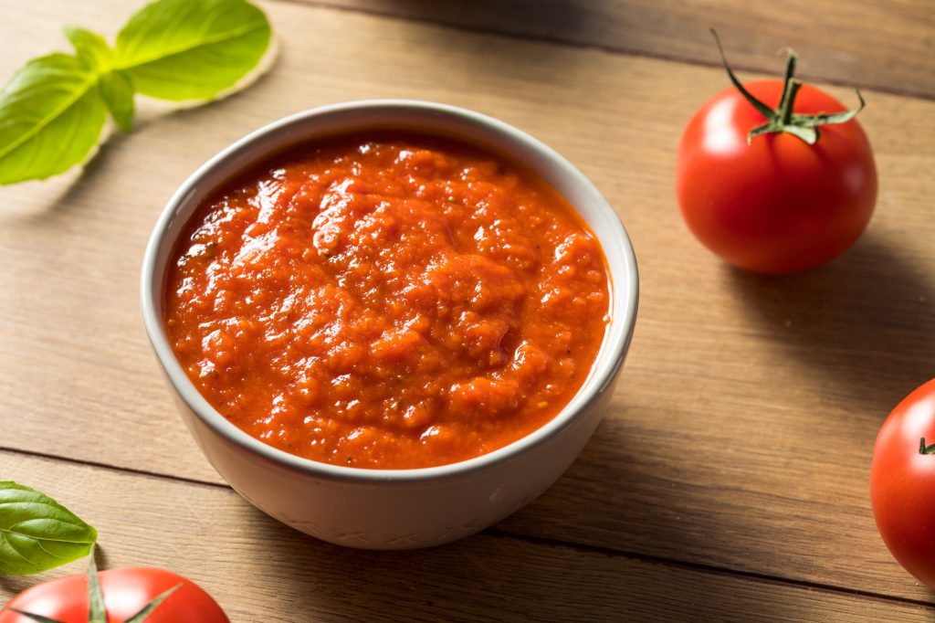 Marinara sauce in a white bowl.  Basil and tomatos beside the bowl.