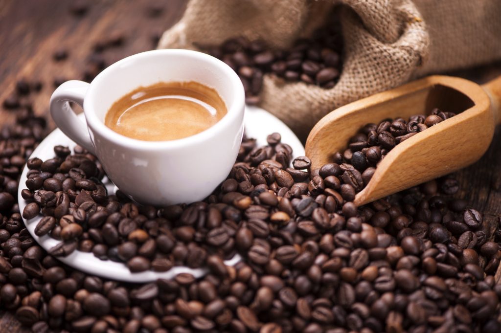 A white cup of espresso surrounded by a lot of coffee beans.