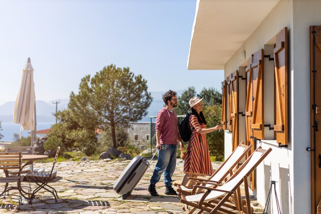 A man and woman with suitcases walking into their airbnb from the outside of building.