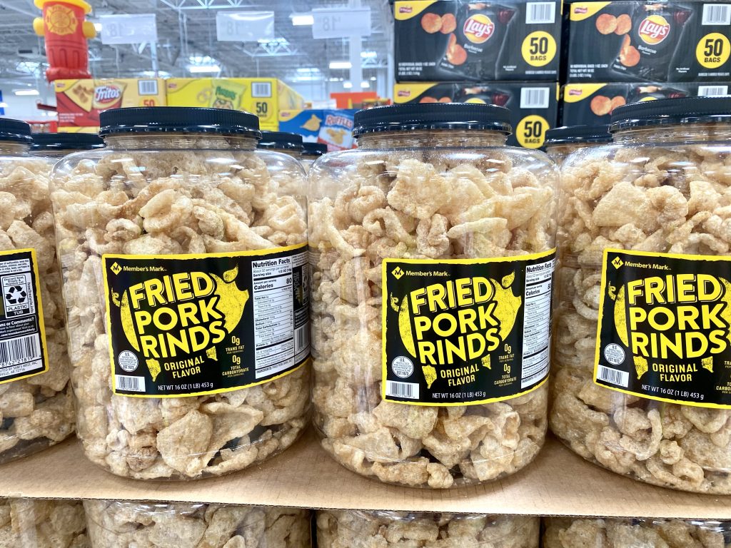 Large plastic containers of pork rinds on grocery shelf.