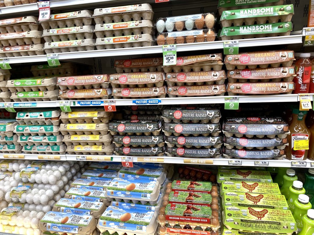 a variety of brands of eggs in the grocery store cooler.