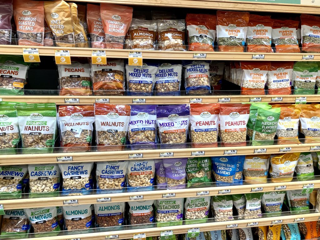 A larger variety of packages of nuts on a grocery shelf.