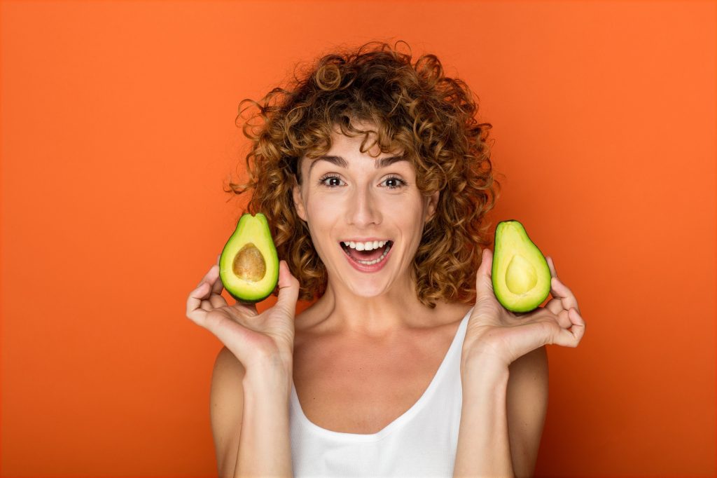 a woman holding a avocado that's been cut in half.