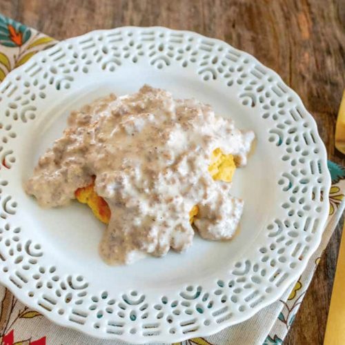 a decorative white plate with low carb biscuits and sausage gravy on it.