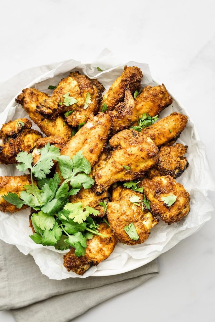 A white platter with crispy curry spiced chicken wings on it.  Garnished with fresh parsley leaves.