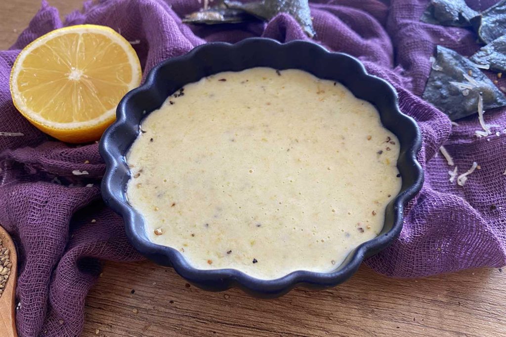 A blue bowl of cheese dip laying on a purple piece of cloth.