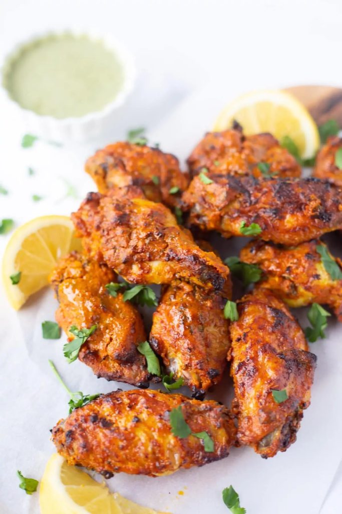 Tandoori Chicken wings on a white platter with wedges of lemon on the side.