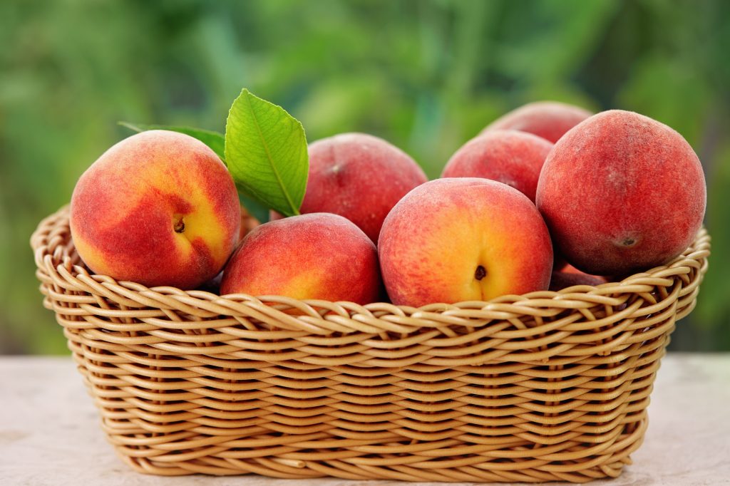 A brown wicker basket full of peaches.