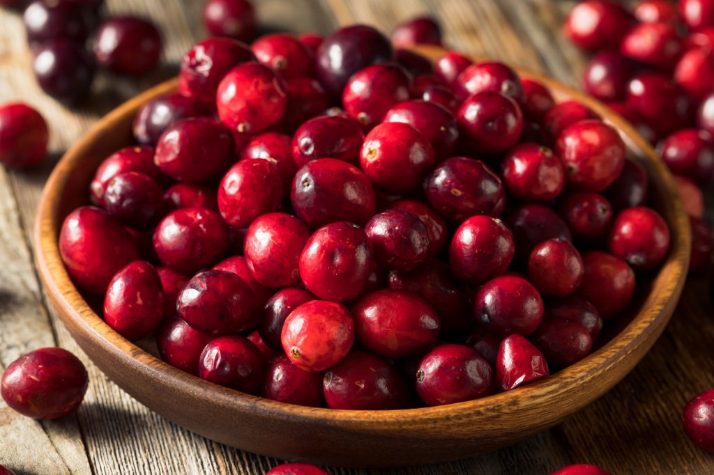 A brown wooden bowlful of cranberries.