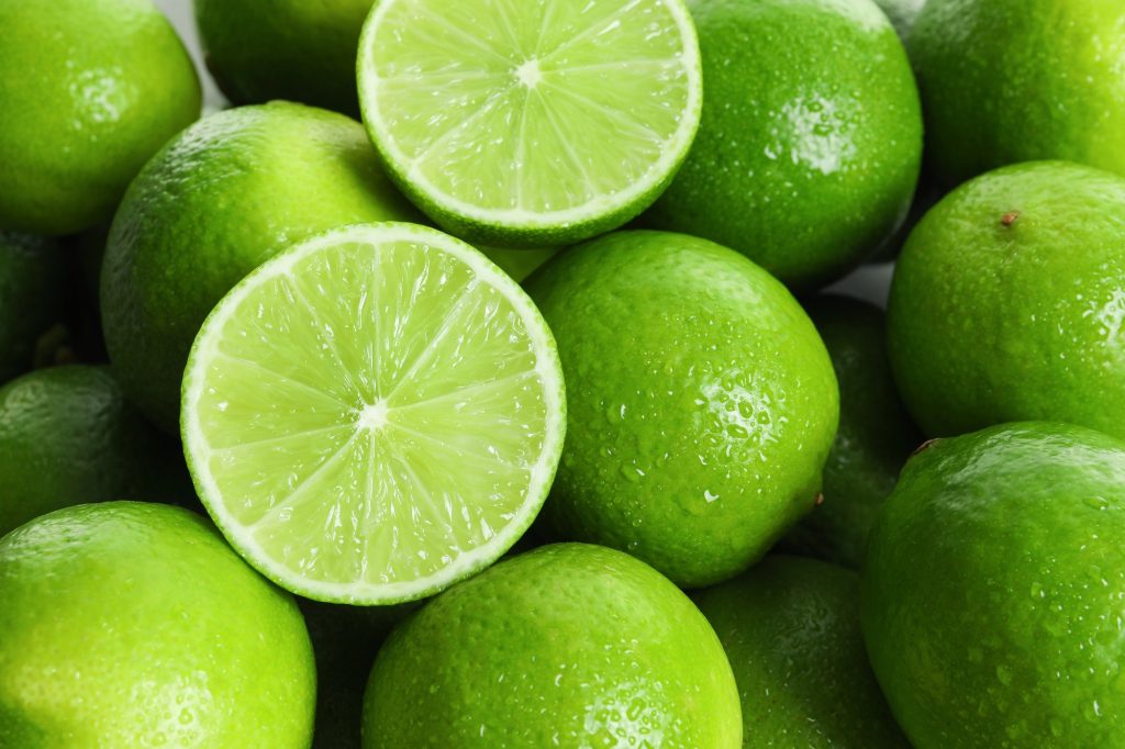 One lime cut in half laying on top of a lot of whole limes.
