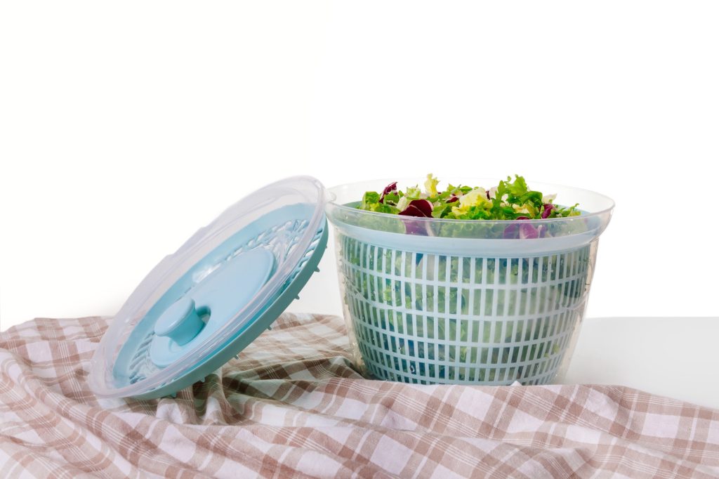 A salad spinner filled with greens on a red and white piece of cloth.