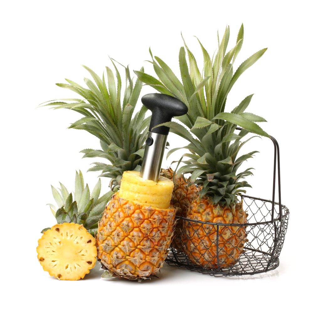 pineapple with a corer sticking out of the middle of it.  Several more whole pineapples.