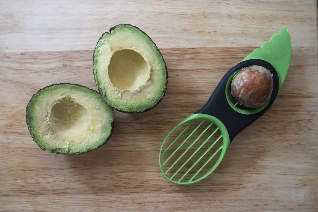 An avocado cut open.  Beside it an avocado slicer tool