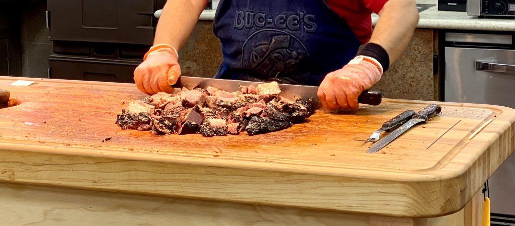 A large wood cutting board with brisket on it, hands chopping the brisket.