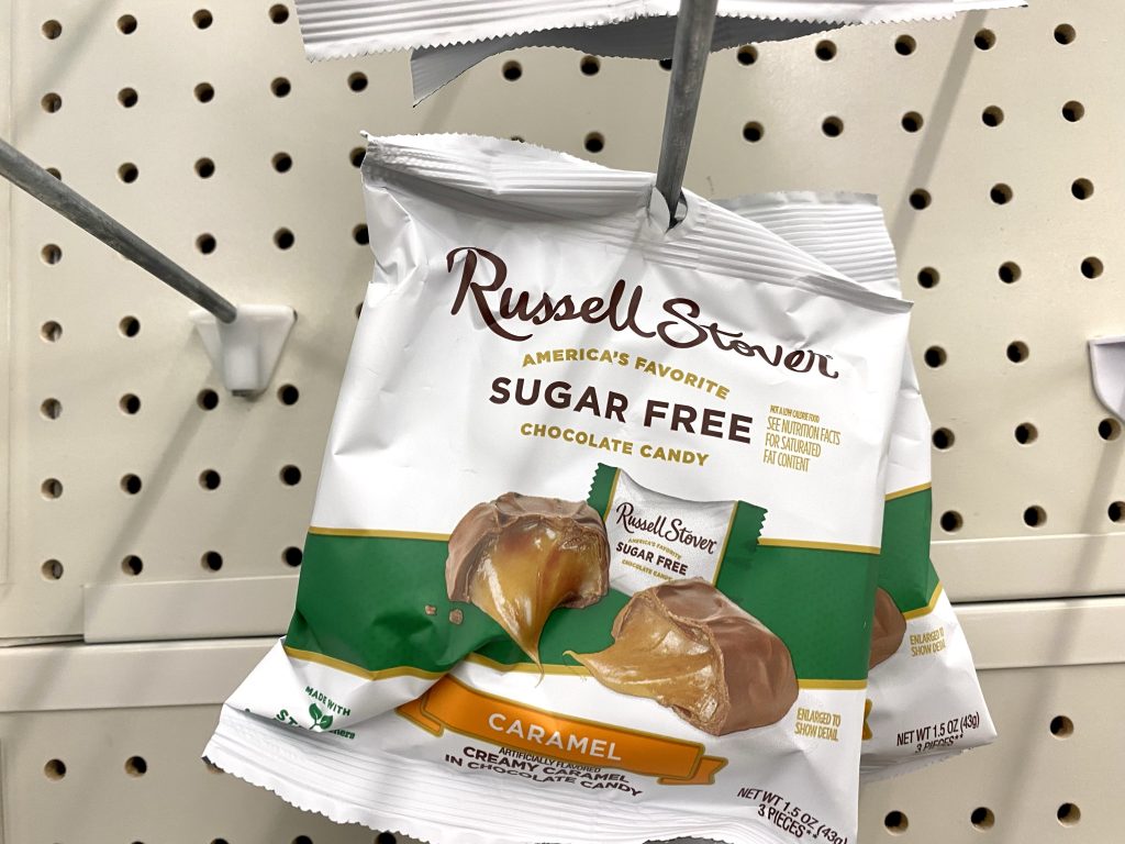 Bags of sugar free chocolate and caramel candy hanging from a hook on store shelf.